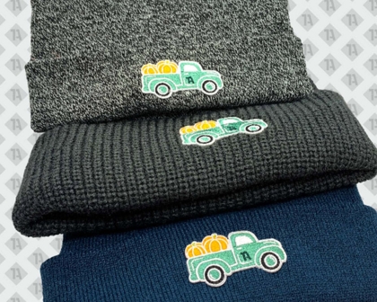 Drei Beanies in Grau, Schwarz und Blau mit gesticktem Patch eines grünen Trucks mit Kürbissen