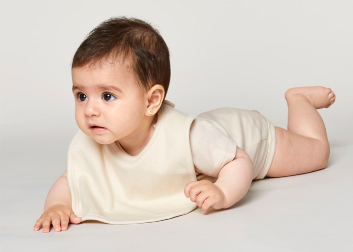 Baby liegt auf dem Bauch und trägt ein helles Lätzchen über dem Body.