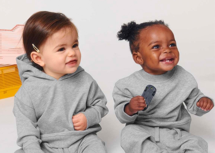 Zwei Babys in grauen Hoodies sitzen nebeneinander und lächeln.