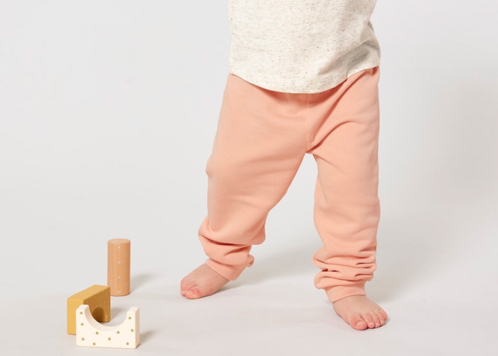 Baby trägt pfirsichfarbene Jogginghose, Spielklötze liegen zu Füßen.