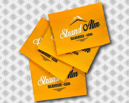 Gewebte Labels „Strand Alm SILBERSEE-LGH“ in Orange mit Bergmotiv