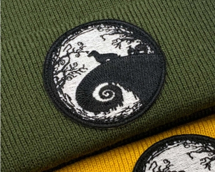 Gestickter runder Patch in Schwarz-Weiß mit mystischem Motiv auf olivgrüner Beanie.