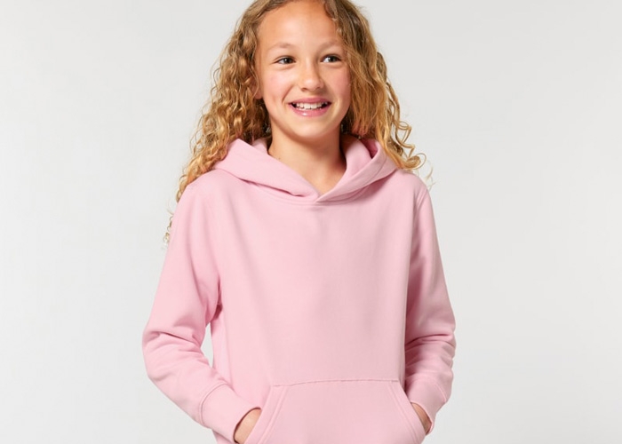 Mädchen steckt die Hände in die Tasche eines rosa Hoodies.