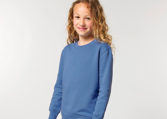 Mädchen mit Locken trägt ein blaues Sweatshirt und lächelt.
