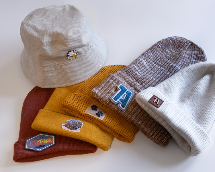 Aufreihung / Fächer von Mützen in herbstlichen Farben mit verschiedenen aufgebrachten Aufnähern und einem Pin